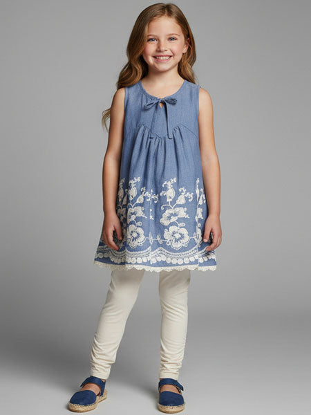 Young girl wearing a blue dress with white embroidery on a gray background
