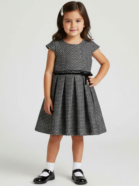 Young girl wearing a black and white patterned dress on a light gray background