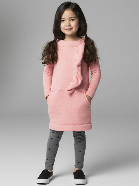 Young girl wearing a pink dress with gray leggings on a gray background