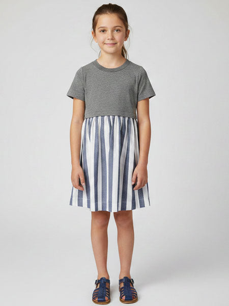 Young girl wearing a gray t-shirt and blue and white striped dress on a white background