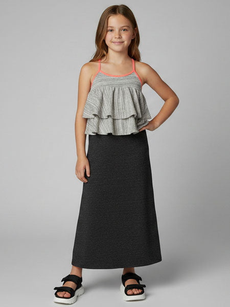 Young girl wearing a gray tiered top and black skirt dress on a gray background