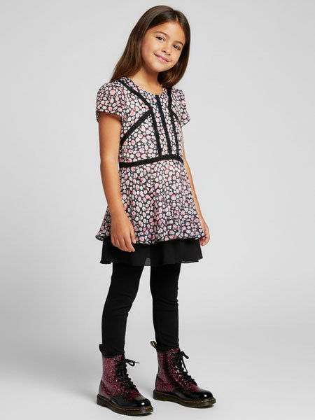 Young girl wearing a heart patterned top, black leggings, and boots on a white background