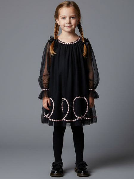Young girl wearing a black dress with sheer sleeves and decorative elements on a gray background