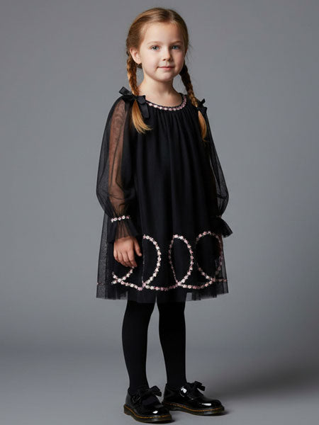 Young girl wearing a black dress with sheer sleeves and white patterns on a gray background