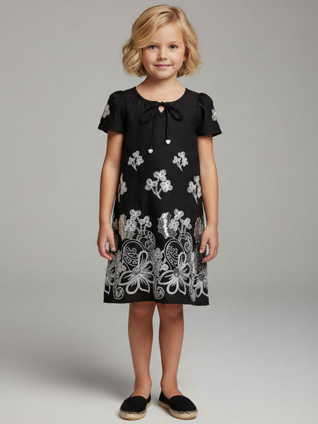 Young girl wearing a black dress with white floral patterns on a plain background