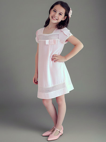 Young girl wearing a light pink dress with lace details on a gray background