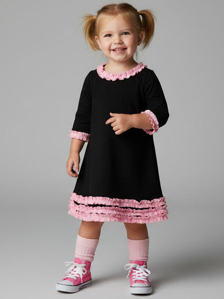 Young girl wearing a black dress with pink trim on a gray background