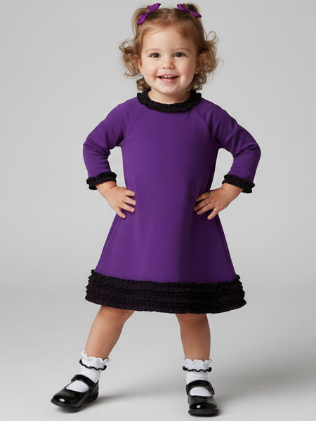 Child wearing a purple dress with black trim on a gray background