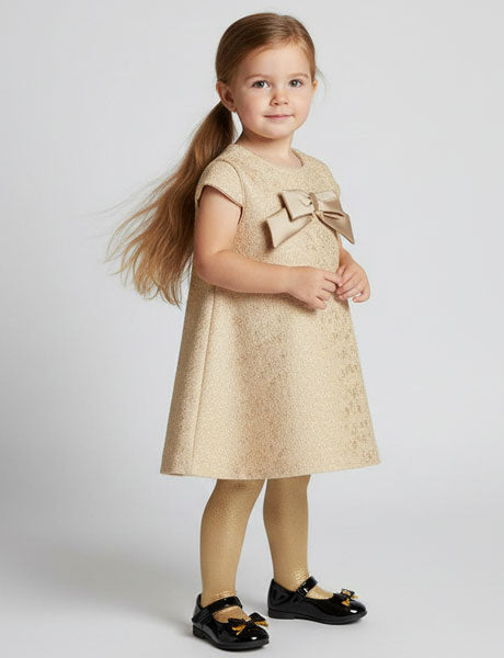 Young girl wearing a beige dress with a large bow on a white background