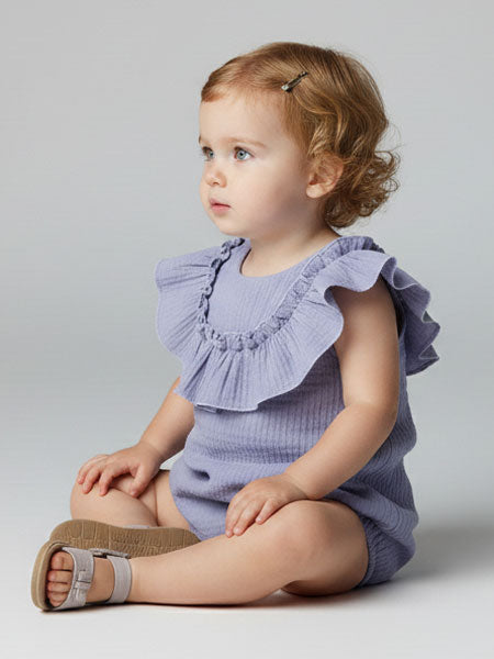 Child wearing a purple ruffled outfit sitting on a light gray background