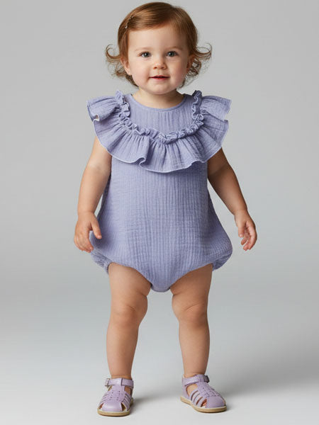 Baby wearing a purple ruffled romper on a plain background