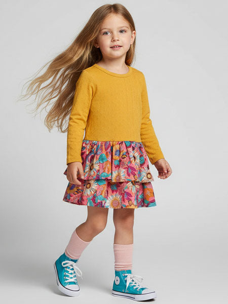 Young girl wearing a mustard yellow dress with colorful floral skirt with blue sneakers on a light gray background