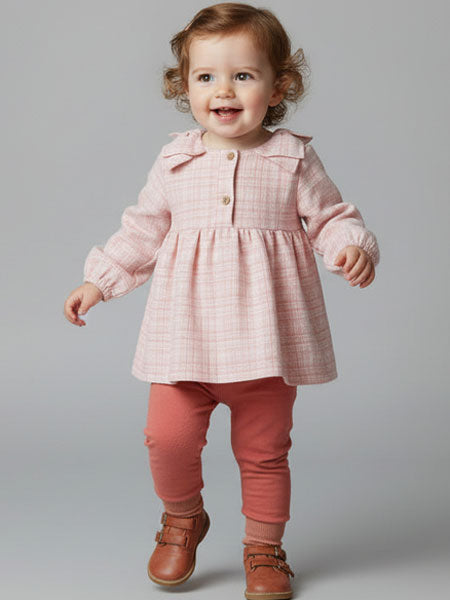 Child wearing a pink checkered dress with a collar, pink pants, and brown shoes on a gray background
