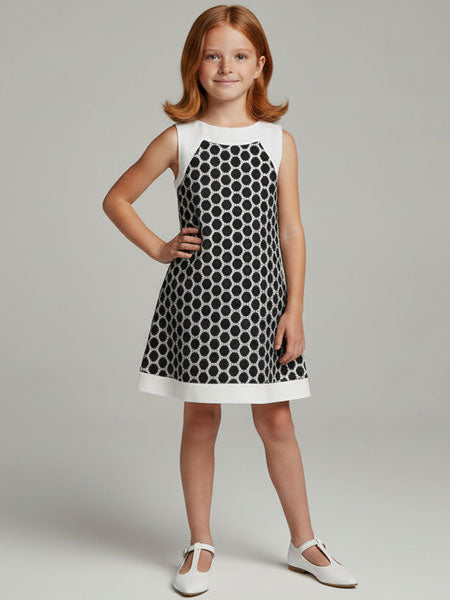 Young girl wearing a black and white polka dot dress with a plain background