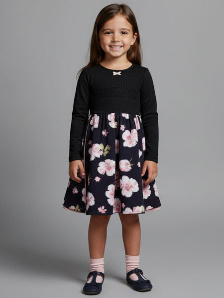 Young girl wearing a black long-sleeve top and floral skirt on a gray background