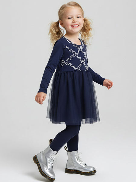 Young girl wearing a navy dress with silver embroidery and silver shoes on a white background