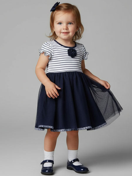 Young girl wearing a striped dress with a navy skirt on a gray background
