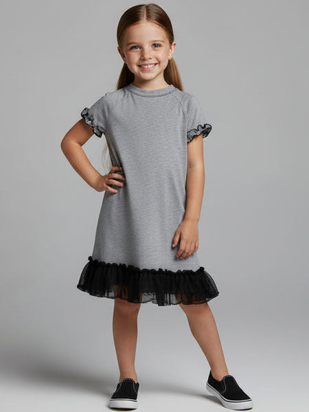 Young girl wearing a gray dress with black ruffled hem on a plain background