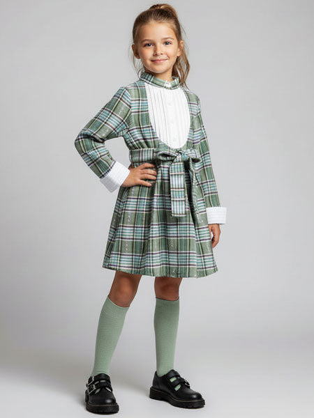 Young girl wearing a green plaid dress with a white shirt and knee-high socks on a gray background