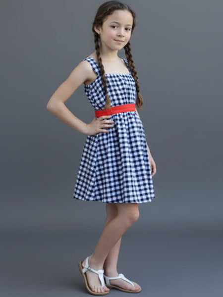 Young girl wearing a blue and white checkered dress with a red belt on a gray background