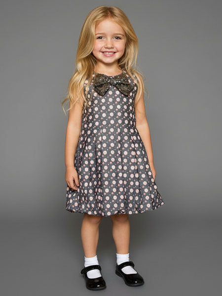 Young girl wearing a floral dress with a large bow on a gray background