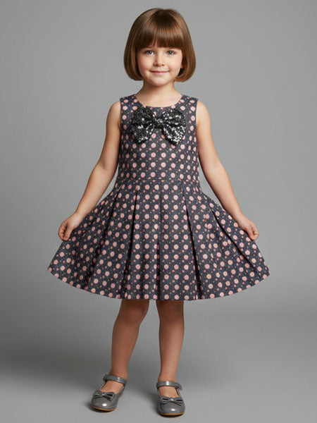 Young girl wearing a polka dot dress with a large bow on a gray background