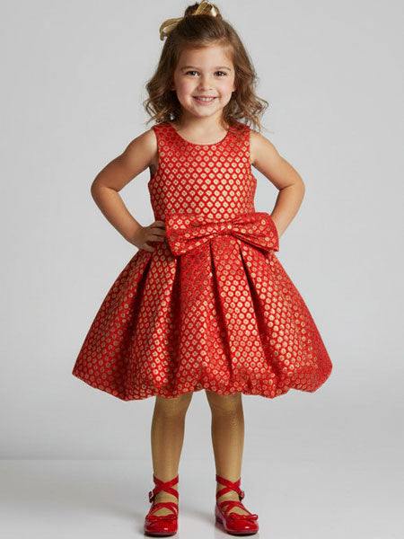 Young girl wearing a red patterned dress with a large bow on a plain background