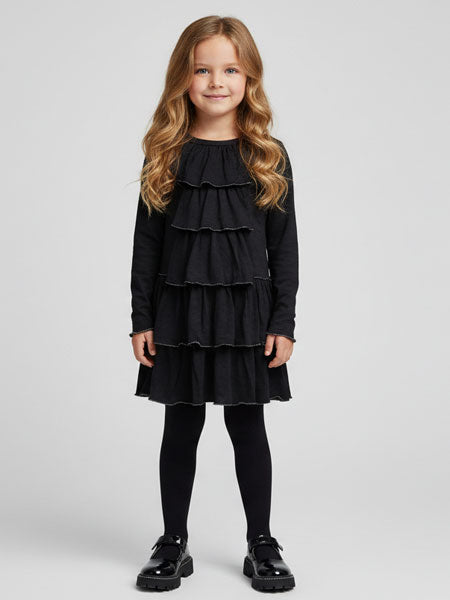 Young girl wearing a black dress with ruffled layers on a white background