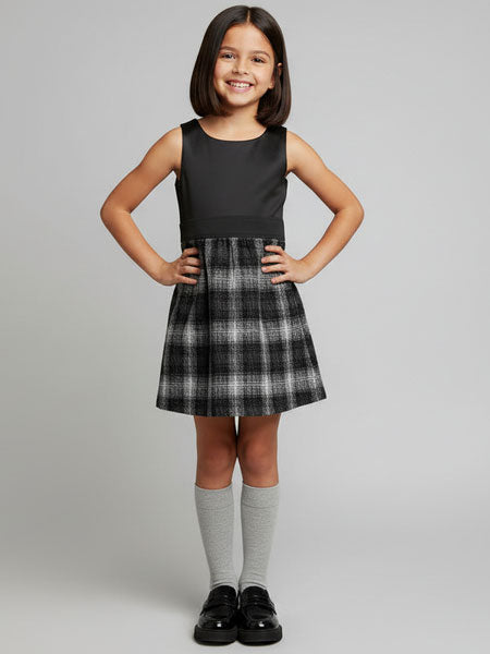 Young girl wearing a black top and plaid skirt dress on a gray background