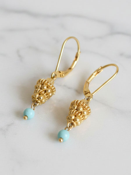 Gold plated earrings with turquoise beads on a marble background