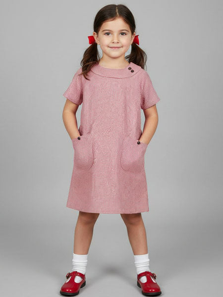 Young girl wearing a red houndstooth dress with red shoes on a gray background