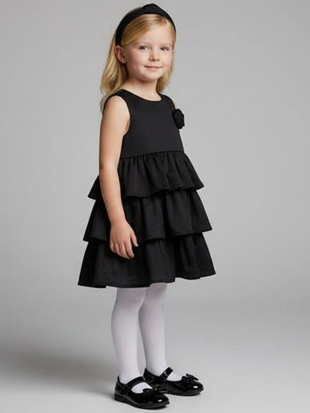 Young girl wearing a black tiered dress on a gray background