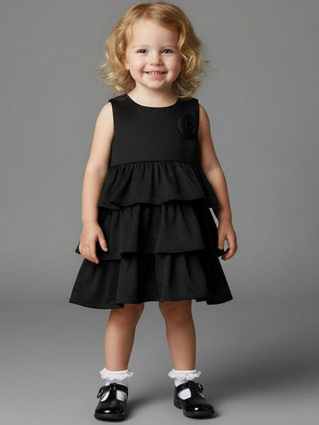 Young girl wearing a black dress with ruffled layers on a gray background