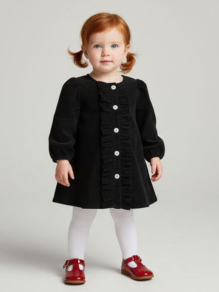 Young girl wearing a black dress with white buttons on a plain background