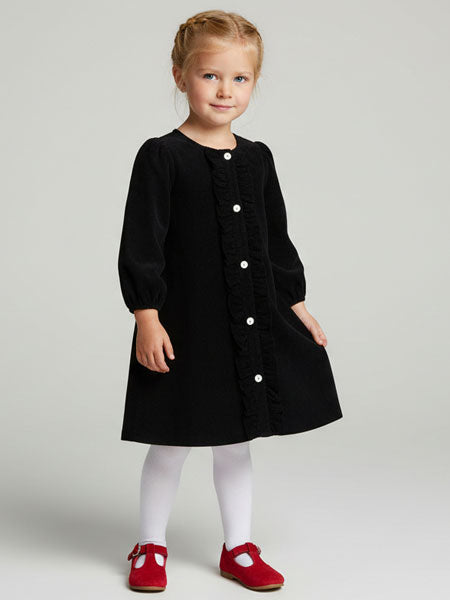 Young girl wearing a black dress with white buttons on a plain background