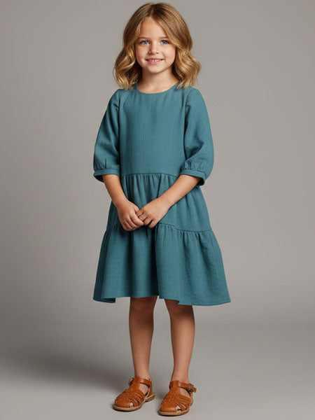 Young girl wearing a teal dress against a gray background