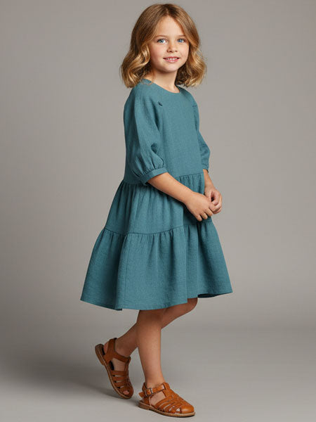 Young girl wearing a teal dress with brown sandals on a gray background