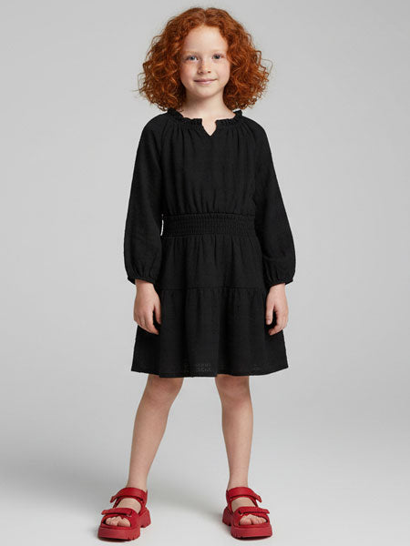 Young girl wearing a black dress with red sandals on a light gray background