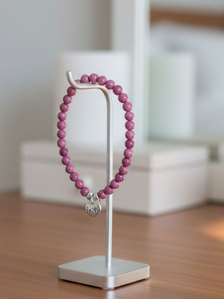 Pink beaded bracelet on a white stand with a blurred background