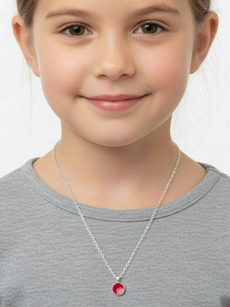 Young girl wearing a necklace with a red pendant on a plain background