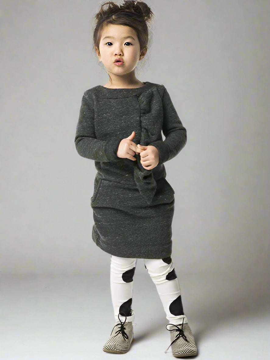 Child wearing a gray dress with  a ruffled from one shoulders on a white background