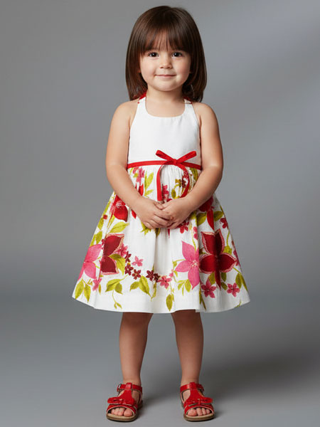 Young girl wearing a floral dress with a red ribbon on a gray background