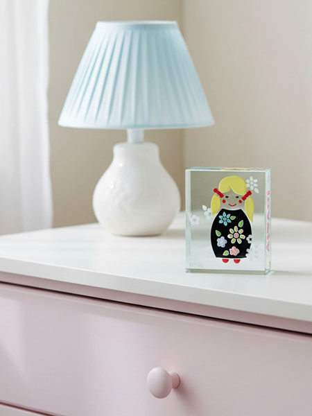 White lamp with pleated blue shade on a white surface next to a clear block with a colorful illustration.