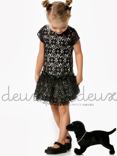 Little girl modeling black lace party dress. Drop waist style with patent leather belt at natural waist. Short cap sleeves, white lining visible under lace.