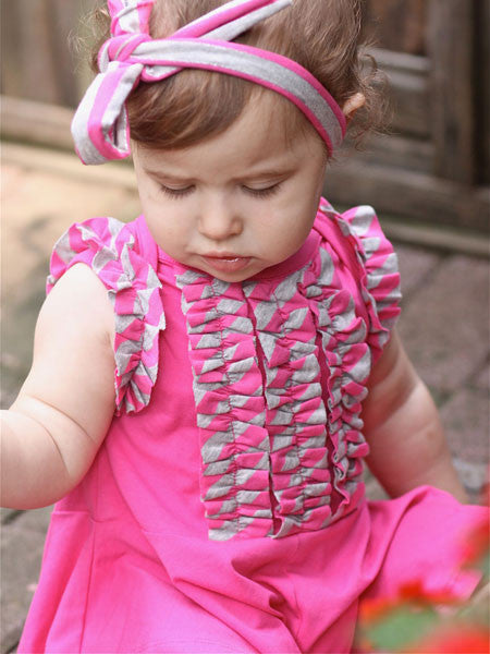Back view, Baby girls one piece romper skort . Raspberry pink. Sleeveless, with gray and pink striped ruffle trim on armholes and down the front to the waist.