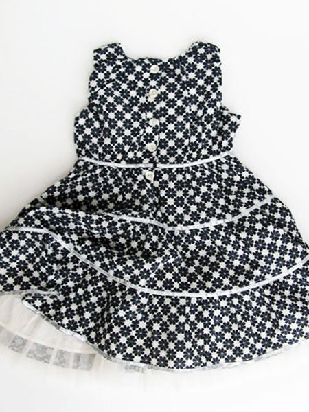 Back of slate gray and white abstract clover print little girls party dress. Tiered. Metallic ribbon and thread accents. Sleeveless. White button closures at center back.